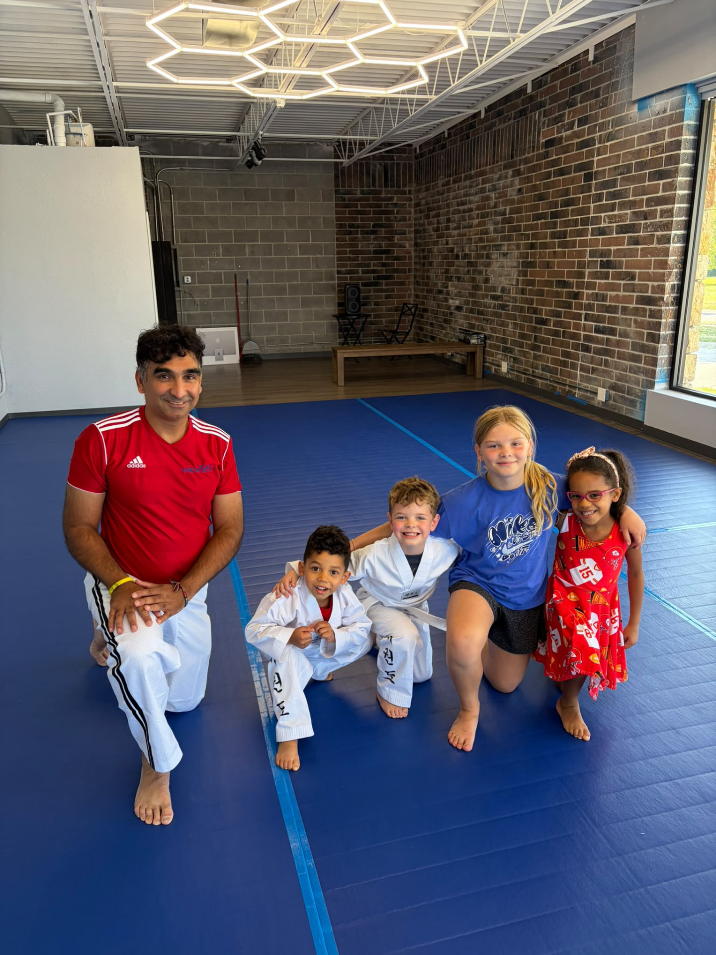 Greg Birring kneeling on the mat with young Kick It Taekwondo students
